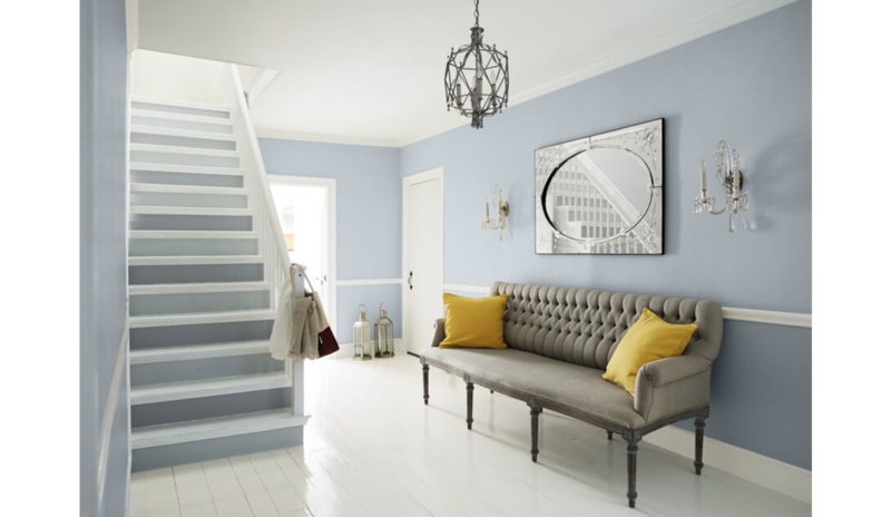 Área de estar azul-gris con escaleras de dos tonos, sofá gris y cojines amarillos, lámpara de araña 