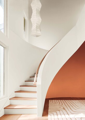 Una escalera curva pintada de color blanquecino, una pared decorativa en naranja intenso debajo