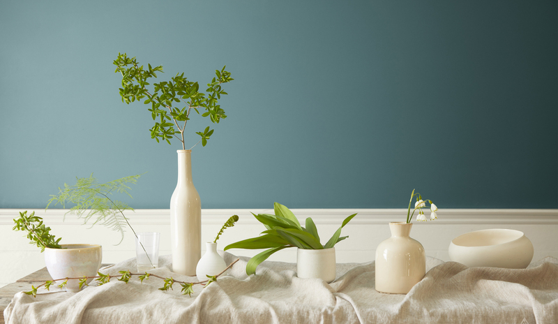 Jarrones blancos y vegetación en una mesa frente a una pared en Aegean Teal 2136-40.