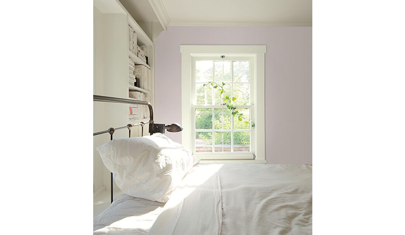 Large bedroom with light pink walls, white built-in shelves, and a metal bedframe with white sheets.