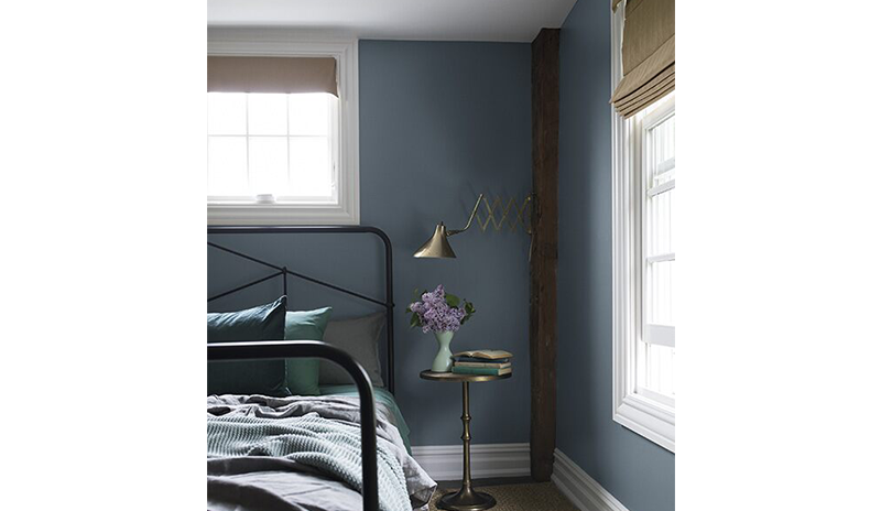 Un dormitorio azul pintado en Black Pepper 2130-40 con vigas de madera vistas y una cama de metal.