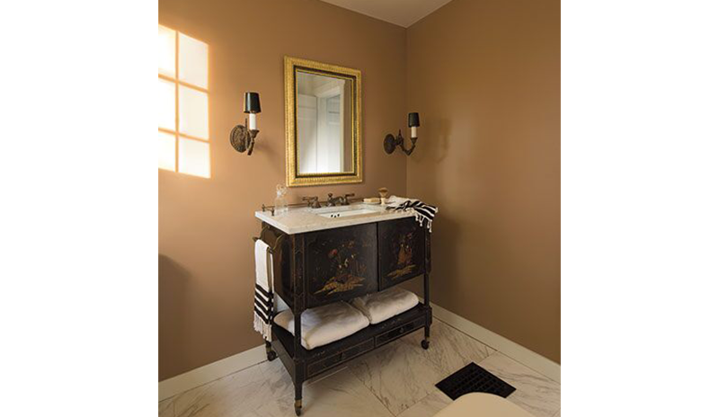Un baño pintado de naranja claro con lavabo clásico, espejos dorados y dos luces de pared.