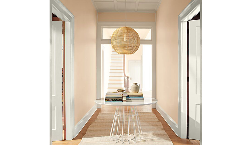 A peach-painted hallway with white doors and trim, rattan ceiling light, modern table, and white rug
