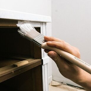 Aplicando imprimación en la superficie de un armario en una habitación con paredes blancas.