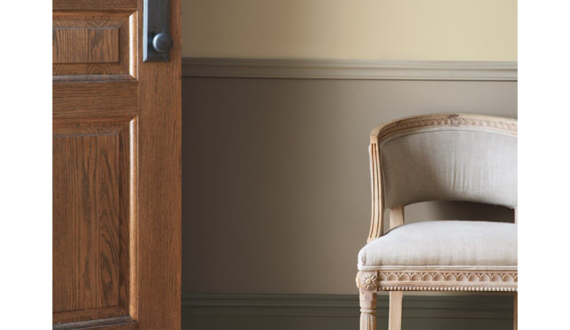Vestíbulo color taupe con puerta de madera, lambriz beige y silla.