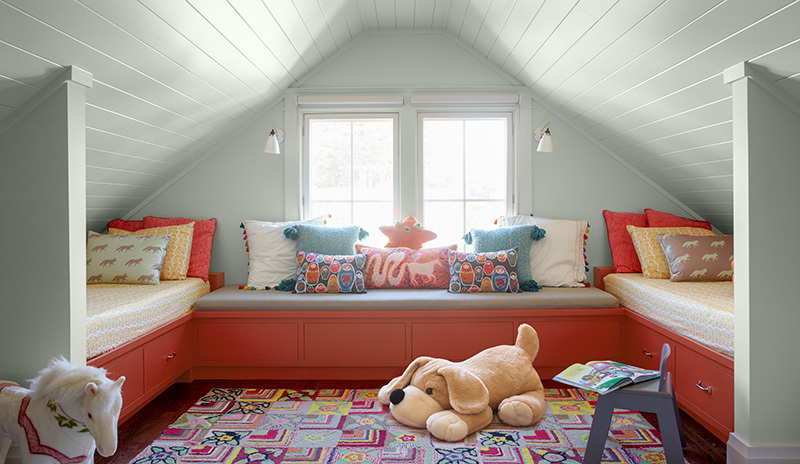 Hab. niños: pared shiplap blanca, 2 camas, sofá en cajones rojos, silla azul, juguetes y cojines.
