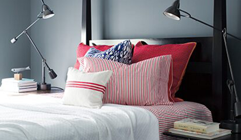 Dormitorio gris lobo elegante c/ cama negra, ropa de cama roja y blanca, 2 lámparas de pared.