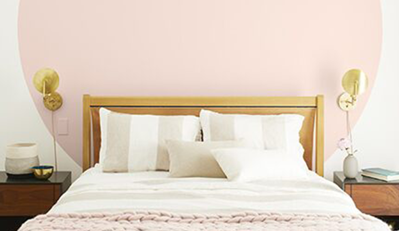 Dormitorio claro con paredes blancas, círculo rosa detrás de la cama blanca con manta rosa y lámpara