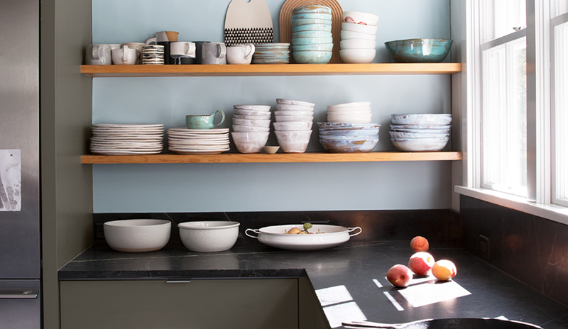 Cocina con 2 estantes de madera que exhiben tazones y platos en una pared de color azul claro.