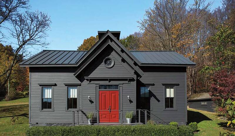 Una casa pintada de gris oscuro con una brillante puerta delantera roja, un seto frontal