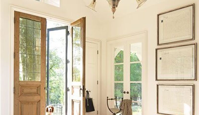 A sunlit, off-white entryway with vaulted ceiling, chandelier, beige and black rug