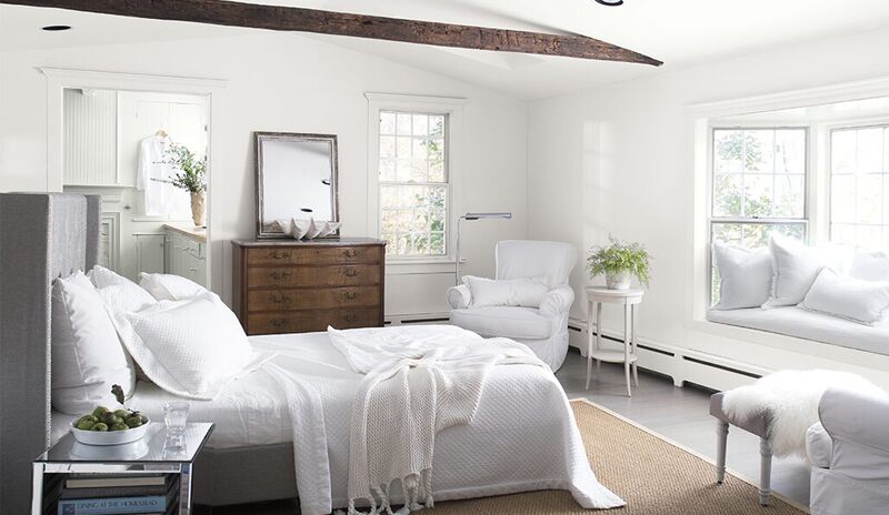 Cozy white bedroom with bedding, chairs, bay window, antique dresser, vaulted ceiling