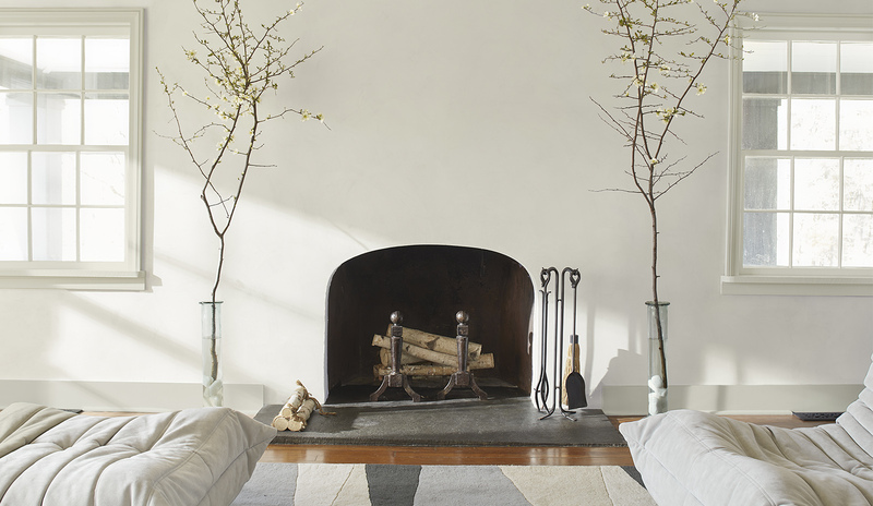 A living room painted in off-white with an arched fireplace flanked by branches in glass vases 