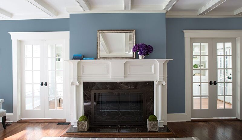 Una chimenea y repisa blancas en una sala de estar azul con puertas dobles acristaladas.