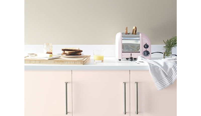 Paredes de color greige con gabinetes de color rosa claro y encimeras blancas en la cocina.