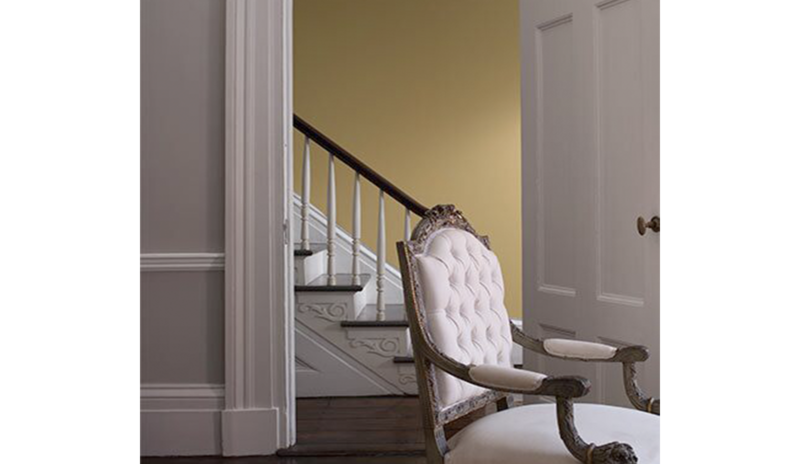 Una sala de estar en gris claro cuenta con una puerta que se abre a un vestíbulo pintado de amarillo