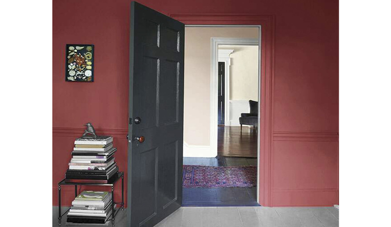 Una pared de color granada con una puerta abierta pintada de gris oscuro y una mesa con libros.