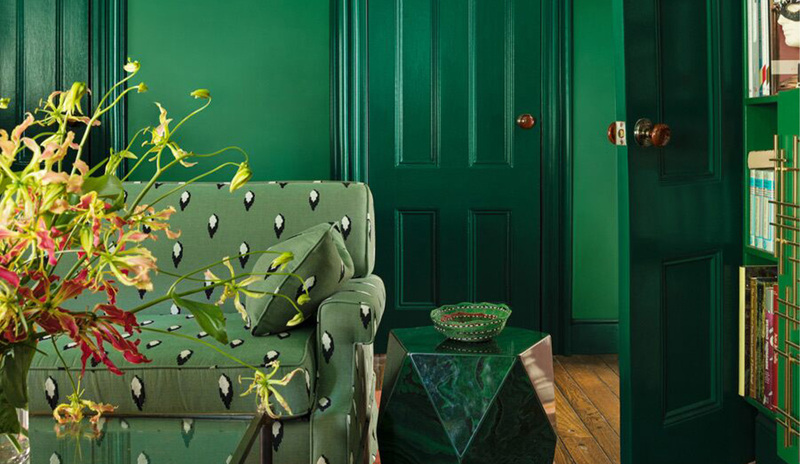 Una sala de estar pintada de verde con un sofá estampado en verde y estanterías iguala a las paredes