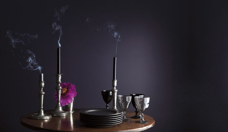 Una mesa de madera ovalada con velas recién apagadas y platos contra una pared de violeta intenso