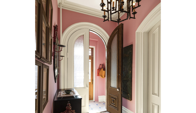 Un pasillo y vestíbulo tradicional con paredes pintadas de rosa, molduras, puertas y techo blancos.