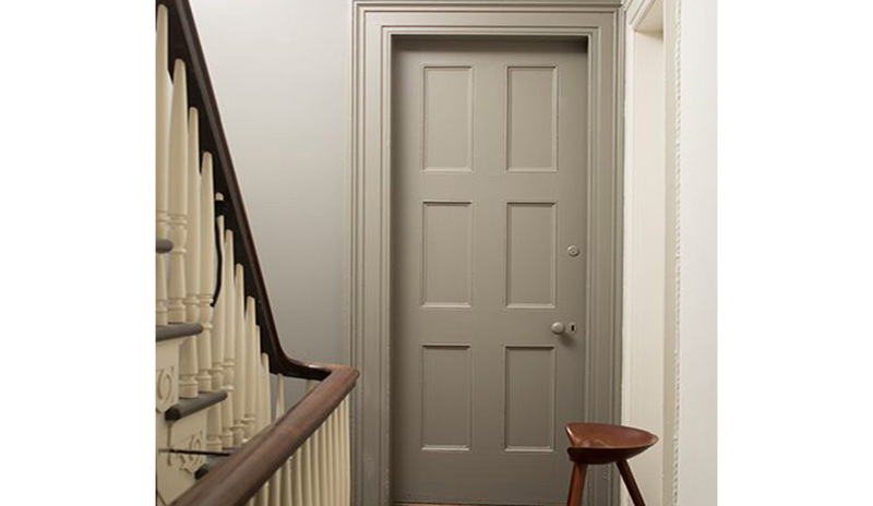 Un pasillo pintado en tonos neutros con piso de madera y una puerta pintada de gris.