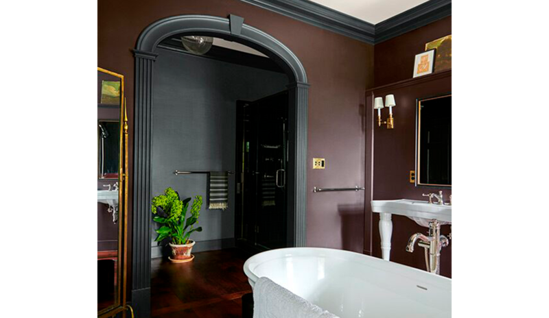 Un gran baño con paredes de color marrón oscuro y molduras negras, bañera profunda y detalles dorado