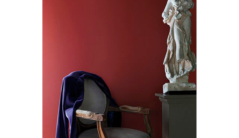 Pared pintada de rojo detrás de una estatua blanca sobre un pedestal y una silla tradicional