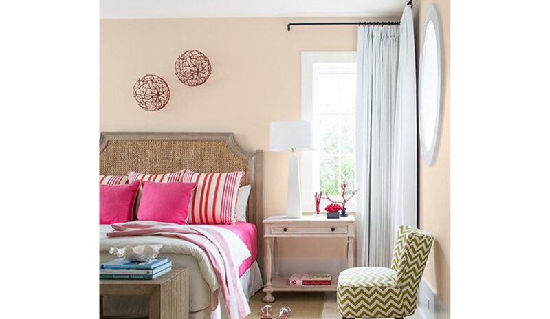 Peach-painted bedroom walls with a green chevron chair, side table, and bed featuring pink bedding.