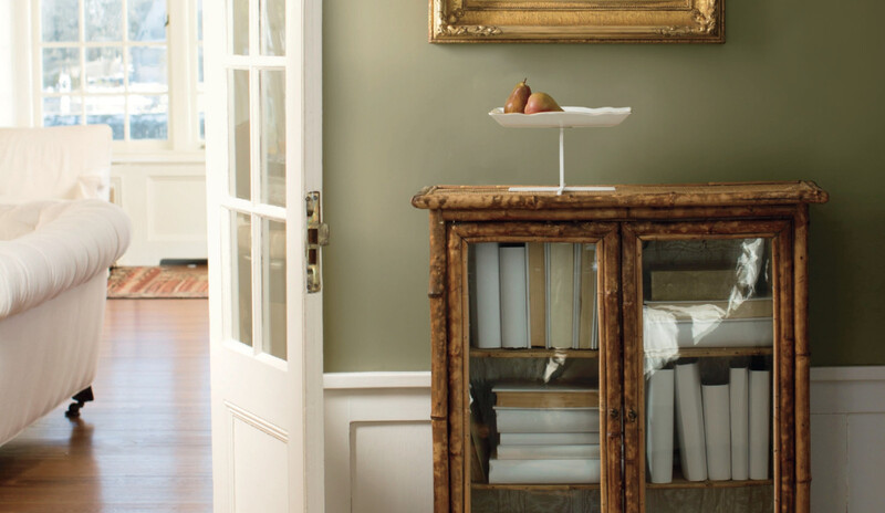 A soft, neutral green accent wall framed by a wooden console