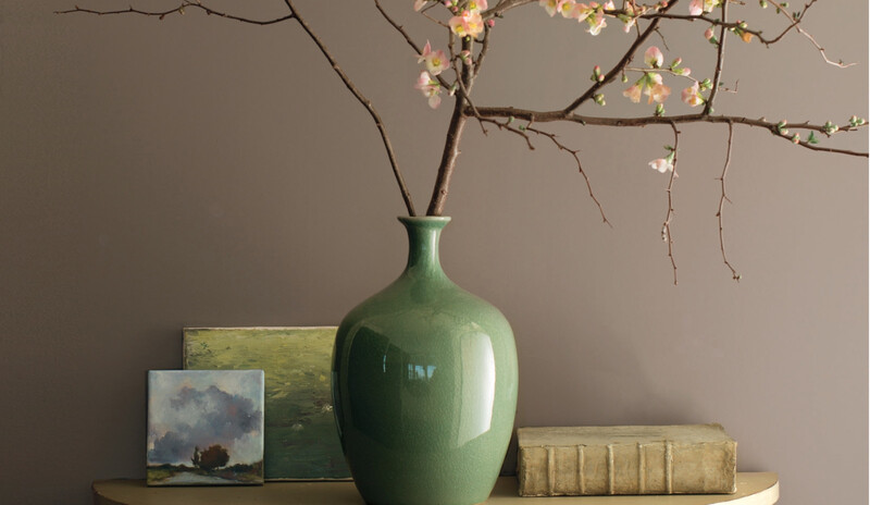 Minimalist floral arrangement in green vase against gray-brown wall.