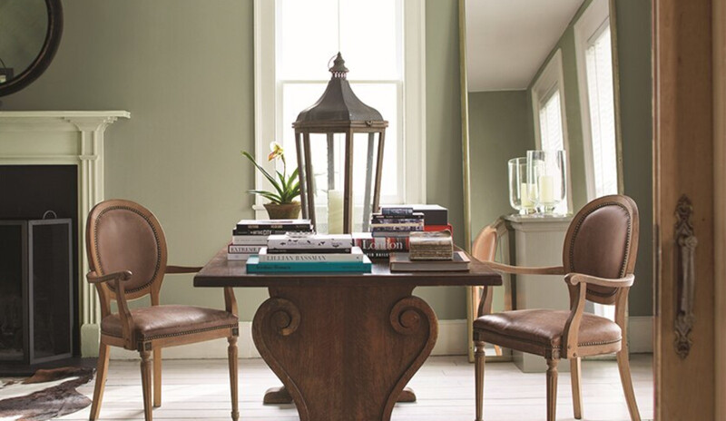 Mesa de madera y dos sillas en una habitación de color verde suave con un espejo de cuerpo entero