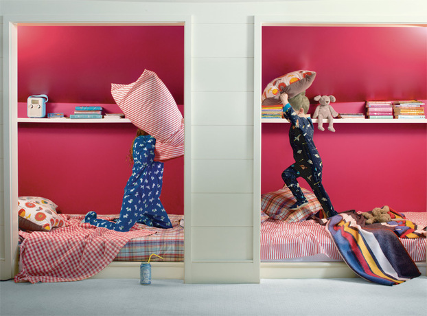 Pintura roja brillante enmarca a dos niños que pelean con almohadas en las camas.