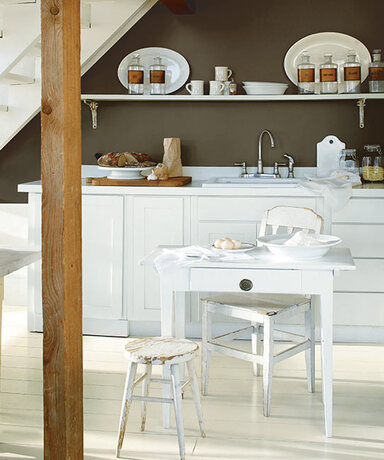 A cozy kitchenette under a white stairway is lovely in a deep neutral wall and white cabinetry.