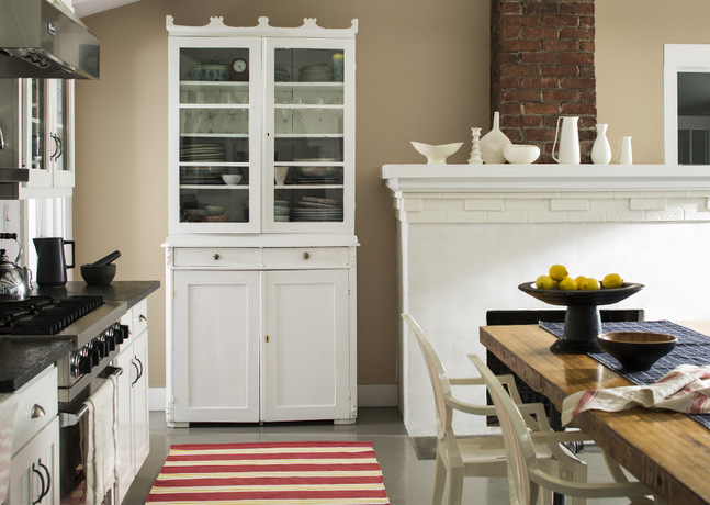 A country kitchen with a white painted fireplace against light brown walls is cozy and welcoming.