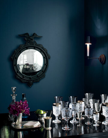 A dark blue-painted dining area with a black mirror on the wall and a table with a glasses