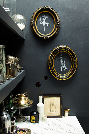 A black-painted room with wall shelves and décor, various glassess, and marble counter.