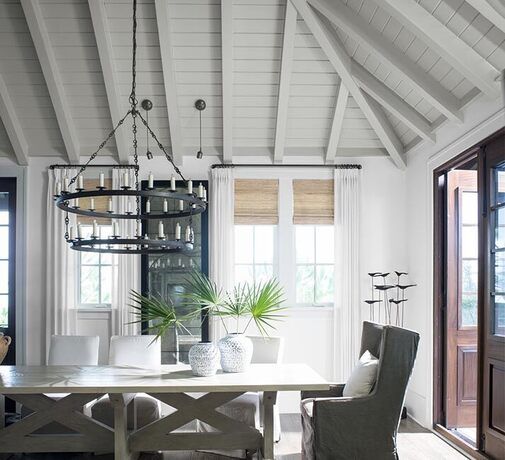A modern white dinning room with wood-paneled ceiling and hanging candle lit chandelier.