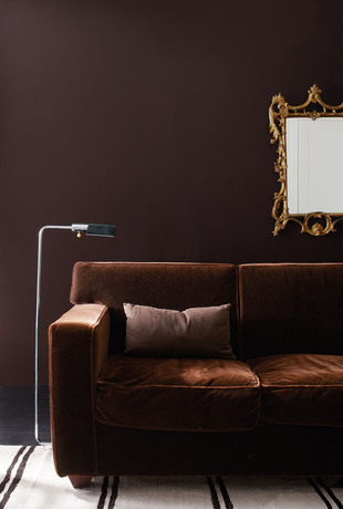 Sala de estar pintada en marrón wengué con espejo dorado en la pared, sofá de terciopelo marrón.