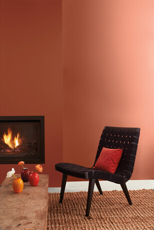 Sala de estar con paredes pintadas de marrón oxidado canela, silla negra y chimenea moderna.
