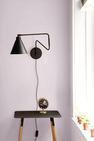 Black wall lamp and table in front of a New Age purple-painted wall.