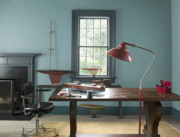 A spacious home office with blue-gray painted walls, a dark gray mantel and trim, a large wood desk
