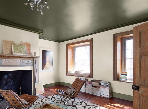 A cozy, sunlit living room with white-painted walls, a dark green ceiling and trim