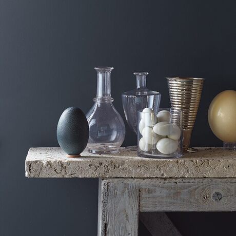 An eclectic mix of vases on a wood bench against a rich navy-painted wall.