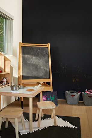 Play area w/ black chalkboard wall, easel, wooden drawing table, felt buckets for toys & shelves.