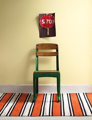 Silla verde, pared amarilla, señal stop pintada y alfombra rayada roja, negra y blanca.