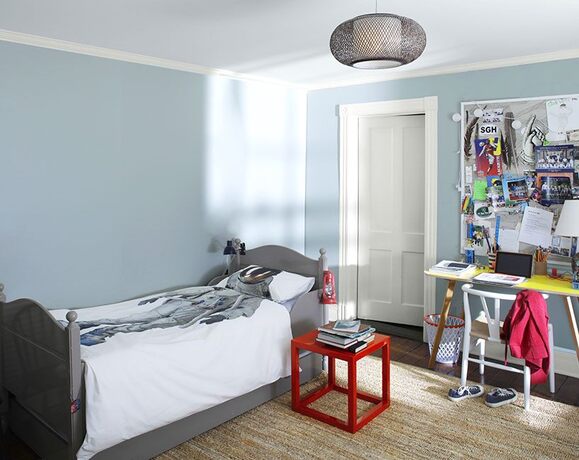 Dormitorio de adolescente con paredes azules, escritorio geométrico, silla, mesa auxiliar