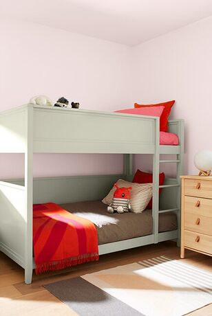 Pink-walled kids' room: bunk beds w/ red and gray bedding, wooden dresser, striped rug.
