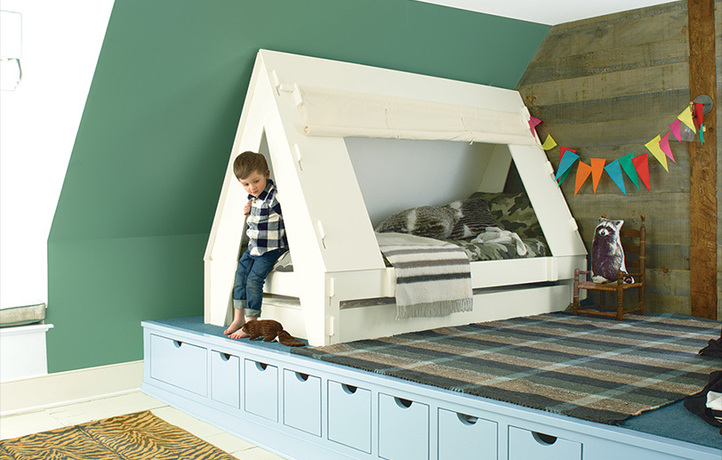 A green-painted angled wall frames a platform with a little boy and his tent bed.