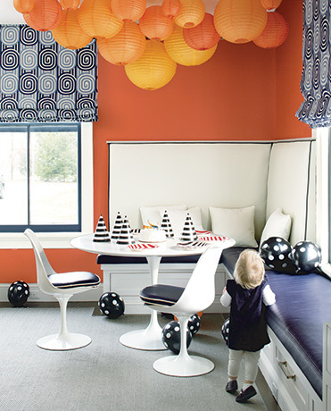 Orange-painted walls and paper lanterns surround a table with birthday hats.