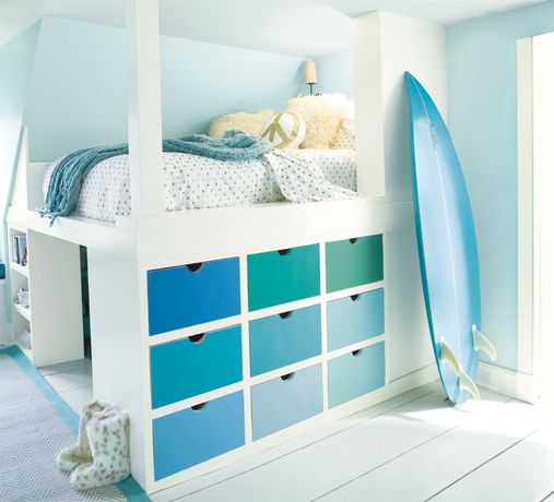 A kid's room with light blue-painted walls features a multi-hued bureau and surfboard.